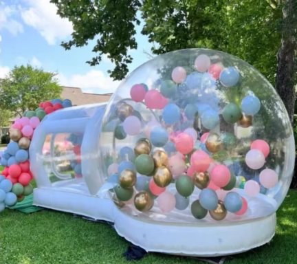 Transparente Hüpfburg mit bunten Ballons in einem Garten.