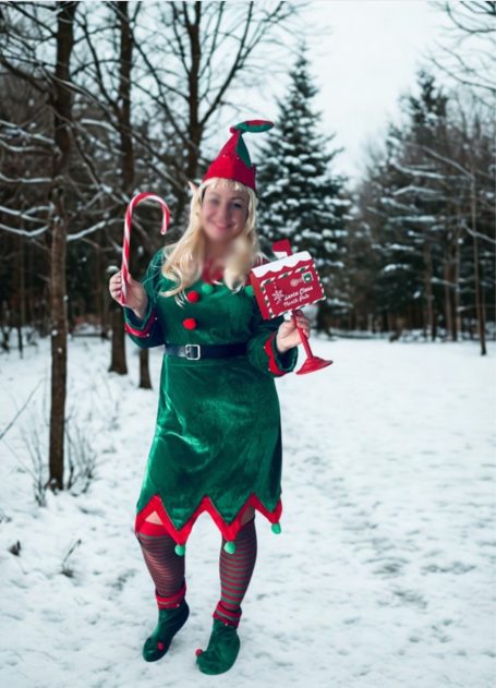 Elfin Eine Person im grünen Weihnachtskostüm mit Zuckerstange und Geschenk in verschneiter Landschaft.
